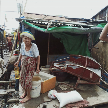 An old resident in the Dagon Seikkan slum area in front of the buckets she uses to collect rainwater for drinking as she does not have the money to buy water